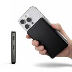 A black power bank held in one hand, with a smartphone partially visible in the background.