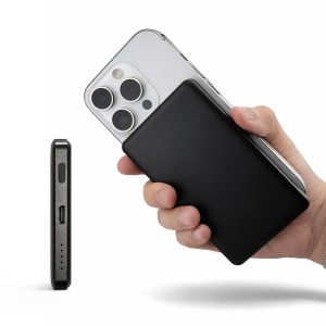A black power bank held in one hand, with a smartphone partially visible in the background.