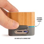 A bamboo Bluetooth speaker featuring a grey base, an SD card slot, a charge port, and flashing coloured lights.