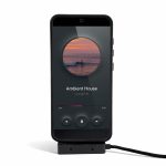 A smartphone displaying a music player interface, connected to a charging cable. The phone is in a protective case.