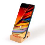 A bamboo phone stand holds a smartphone at an angle, featuring a simple design with a logo on the base.