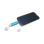 A USB flash drive in turquoise connected to a smartphone, with two small caps beside it.