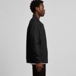 A man in a black bomber jacket stands sideways, showcasing the jacket's design and fit. The jacket has a logo.