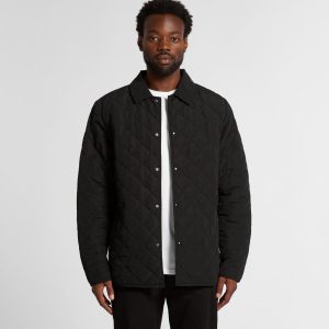A man wearing a black quilted jacket with a button-up front and a collared neck. The jacket has a logo.